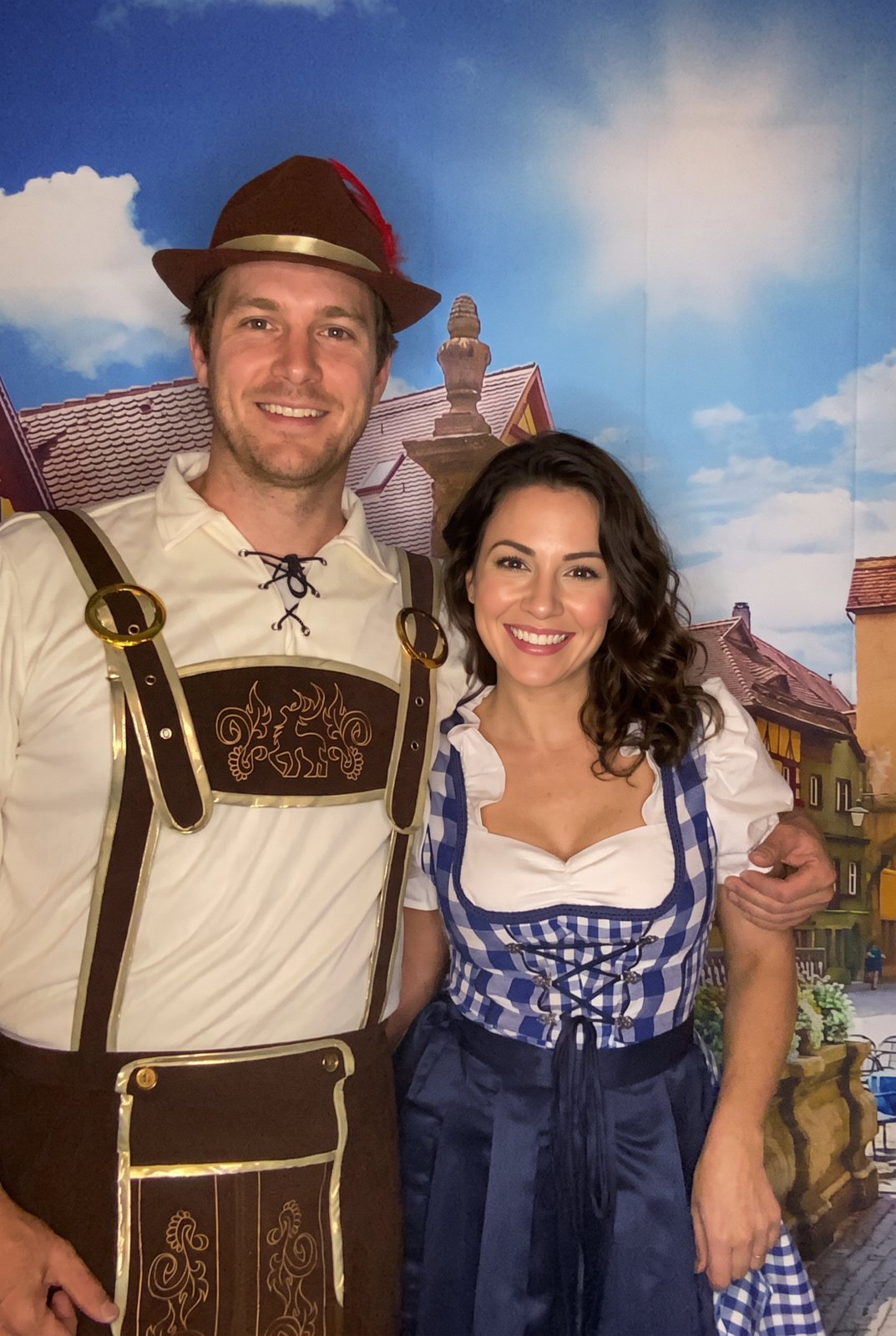Couple in lederhosen and a dirndl posing in front of a Bavarian village backdrop